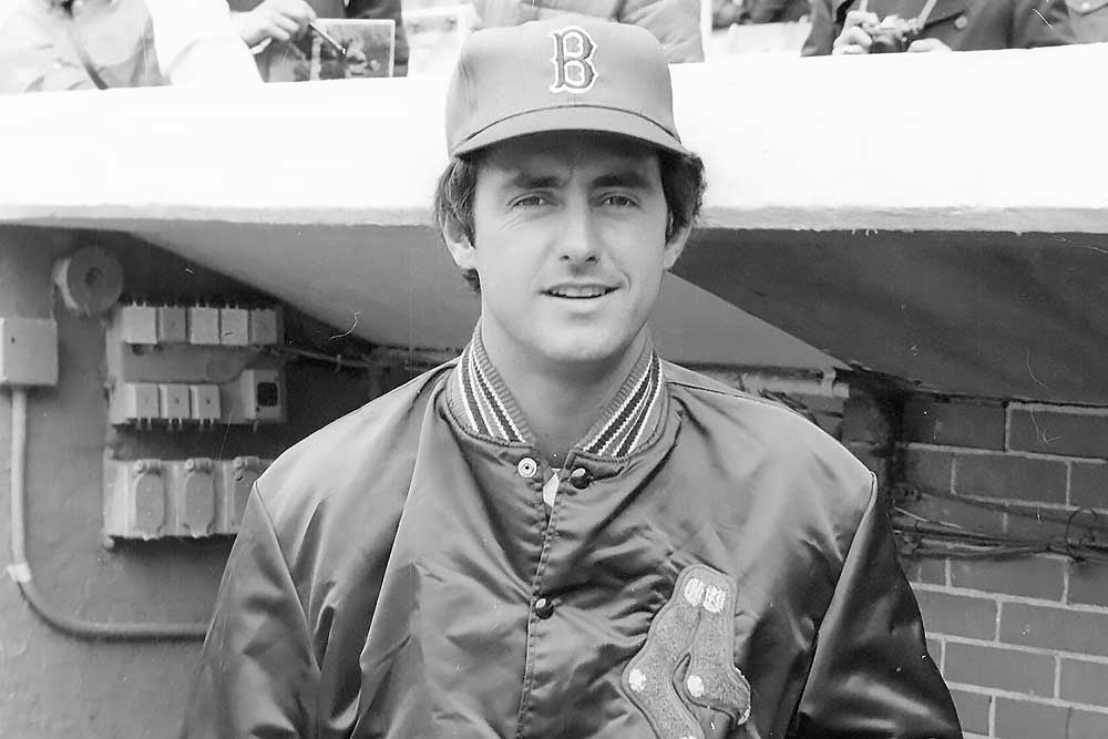 A young man in a Boston Red Sox jacket and cap stands in a dugout, smiling. The image is from the Fred Lynn official website, highlighting his time as a center fielder and 1975 MVP in Major League Baseball.| Fredlynn.com | Official Home of Fred Lynn